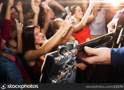 holidays, music, nightlife and people concept - close up of musiciab playing electric guitar on stage over happy people crowd taking picture by smartphones and waving hands at concert in night club