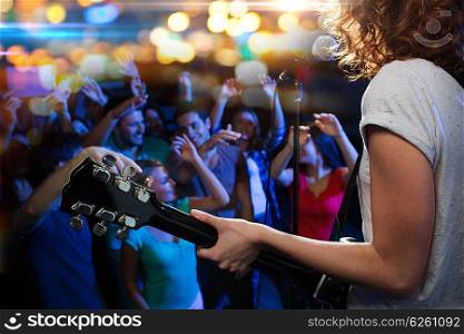 holidays, music, nightlife and people concept - close up of singer playing electric guitar and singing on stage over happy fans crowd waving hands at concert in night club