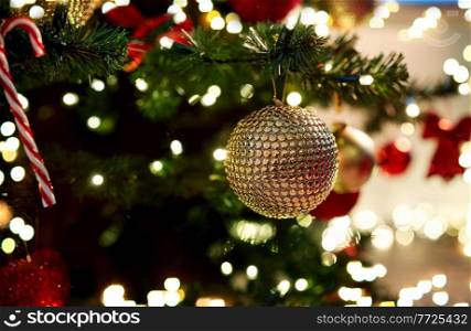 holidays, new year and celebration concept - golden christmas ball decoration hanging on artificial fir tree. golden christmas ball decoration on fir tree