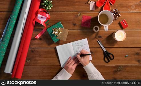 holidays, new year and christmas concept - female&rsquo;s hands writing to do list in notebook on wooden table. hands writing to do list in notebook on christmas