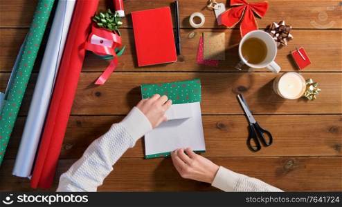 holidays, new year and christmas concept - hands wrapping gift box into green paper on wooden table. hands wrapping christmas gift into paper at home