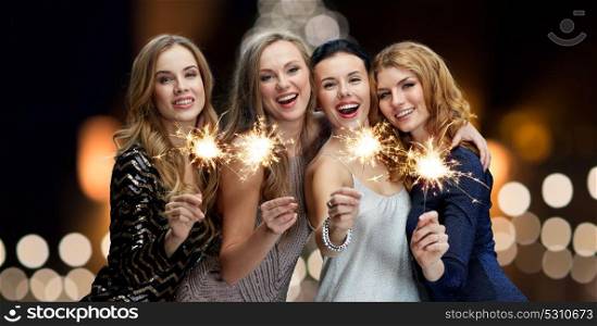 holidays, new year and people concept - happy young women with sparklers over christmas tree lights background. happy young women with sparklers at new year night