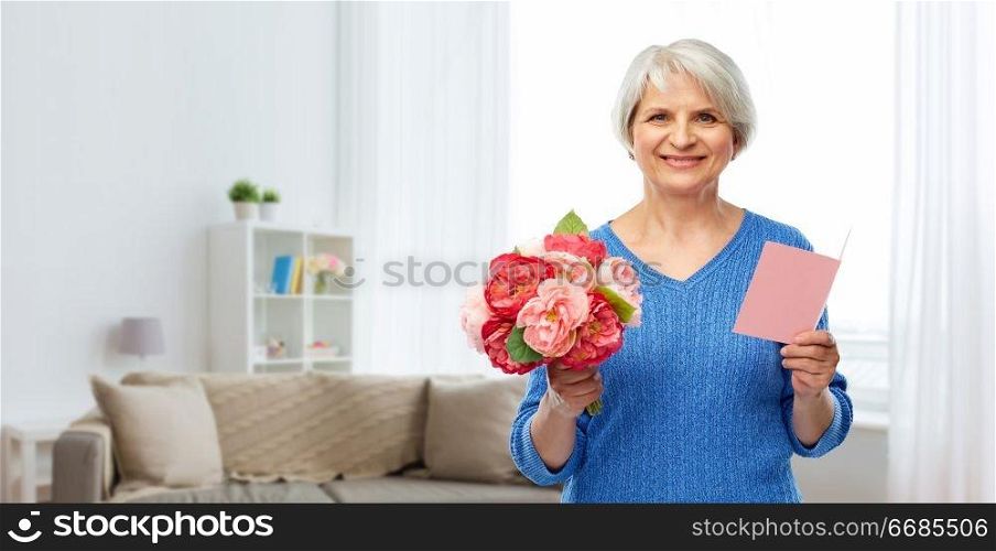 holidays, old age and international women&rsquo;s day concept - happy smiling senior woman with flowers and greeting card over home living room background. happy senior woman with flowers and greeting card