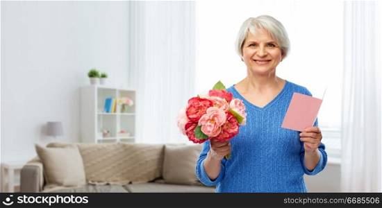 holidays, old age and international women&rsquo;s day concept - happy smiling senior woman with flowers and greeting card over home living room background. happy senior woman with flowers and greeting card