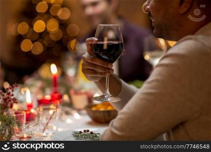 holidays, party and celebration concept - close up of happy smiling man having christmas dinner at home and drinking red wine. close up of man drinking wine at christmas party