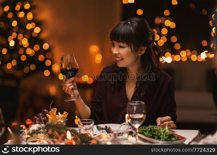holidays, party and celebration concept - happy asian woman having christmas dinner at home and drinking red wine. happy asian woman drinking wine at christmas party