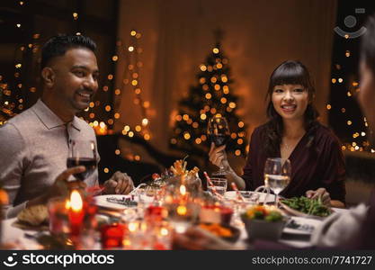 holidays, party and celebration concept - happy friends having christmas dinner at home and drinking wine. happy friends drinking wine at christmas party