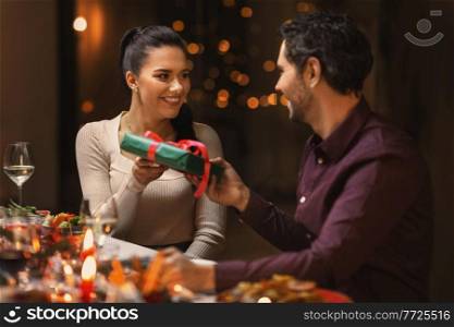 holidays, party and celebration concept - happy friends or couple having christmas dinner and giving presents at home. happy friends giving christmas presents at home