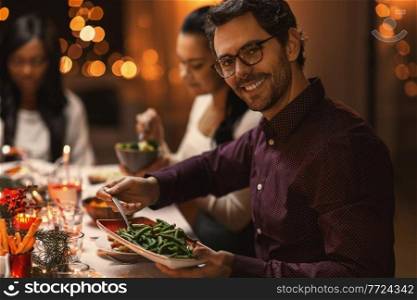 holidays, party and celebration concept - happy man with friends having christmas dinner at home. happy man with friends having christmas dinner