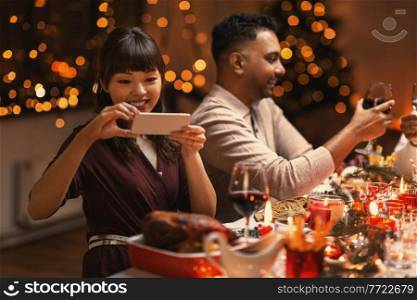 holidays, party and celebration concept - happy smiling asian woman having christmas dinner with friends and photographing food at home. happy woman photographing food at christmas dinner