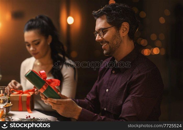holidays, party and celebration concept - happy smiling man with gift box on christmas dinner at home. happy smiling man with christmas gift at home