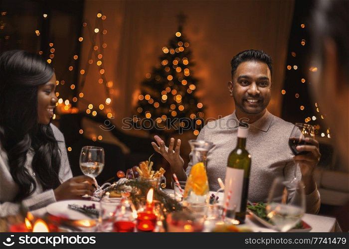 holidays, party and celebration concept - multiethnic group of happy friends having christmas dinner at home and drinking wine. happy friends drinking wine at christmas party