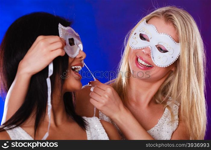 Holidays, people and celebration concept. Closeup two women face african and caucasian with white silver carnival masks