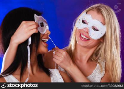 Holidays, people and celebration concept. Closeup two women face african and caucasian with white silver carnival masks