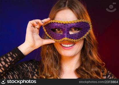 Holidays, people and celebration concept. Closeup woman face with carnival violet mask on dark background.. Closeup woman face with carnival violet mask on dark