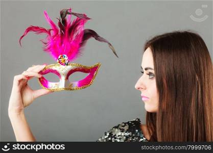 Holidays, people and celebration concept. Closeup woman holding pink carnival venetian mask in hand on gray background.