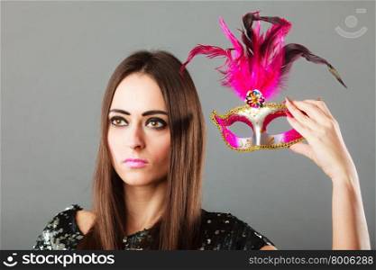 Holidays, people and celebration concept. Closeup woman holding pink carnival venetian mask in hand on gray background.