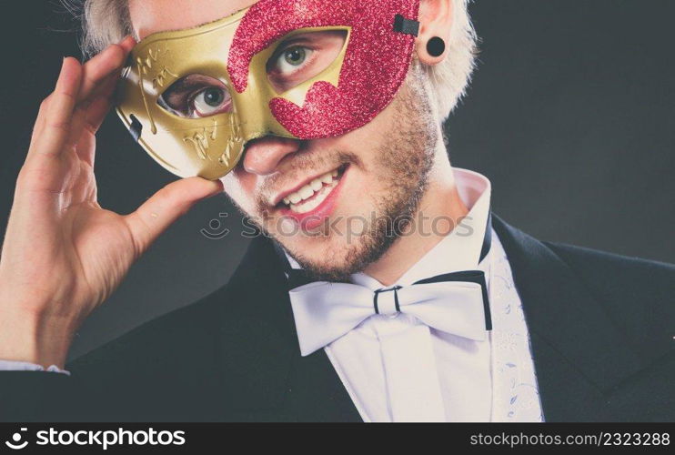 Holidays, people and celebration concept. Elegant young guy wearing suit white shirt bow tie and carnival venetian mask, on dark.. Young man in carnival mask on dark