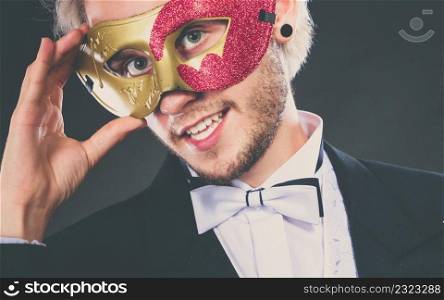 Holidays, people and celebration concept. Elegant young guy wearing suit white shirt bow tie and carnival venetian mask, on dark.. Young man in carnival mask on dark