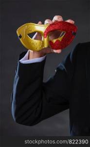 Holidays, people and celebration concept. Male hand holding red golden carnival mask closeup on dark. Male hand holds carnival mask closeup