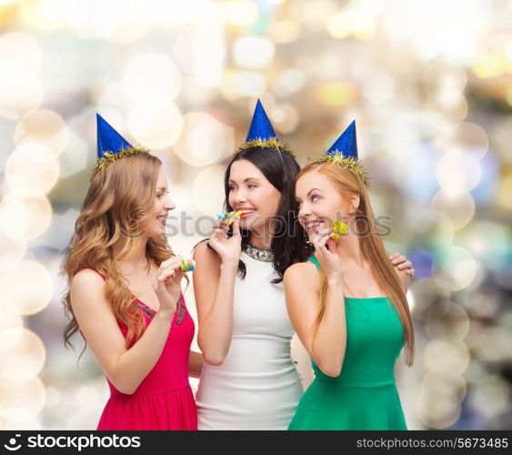 holidays, people and celebration concept - smiling women in party caps blowing to whistles over lights background