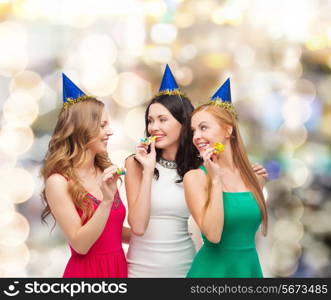 holidays, people and celebration concept - smiling women in party caps blowing to whistles over lights background