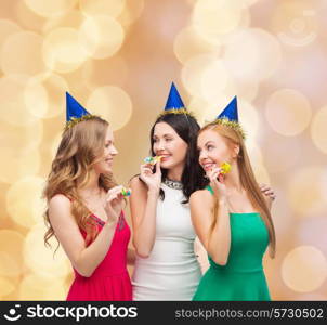 holidays, people and celebration concept - smiling women in party caps blowing to whistles over beige lights background