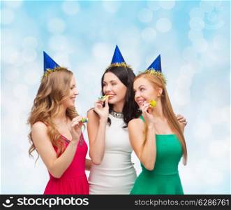 holidays, people and celebration concept - smiling women in party caps blowing to whistles over blue lights background