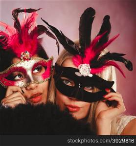 Holidays, people and celebration concept. two women mixed race and caucasian with carnival venetian masks and black feather fan