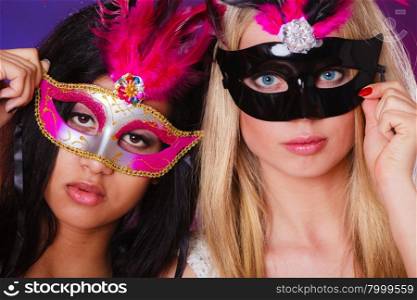 Holidays, people and celebration concept. two women mixed race and caucasian with carnival venetian masks over festive background.
