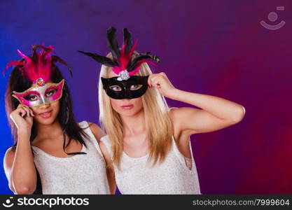 Holidays, people and celebration concept. two women mixed race and caucasian with carnival venetian masks over festive background.