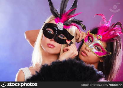 Holidays, people and celebration concept. two women mixed race and caucasian with carnival venetian masks and black feather fan