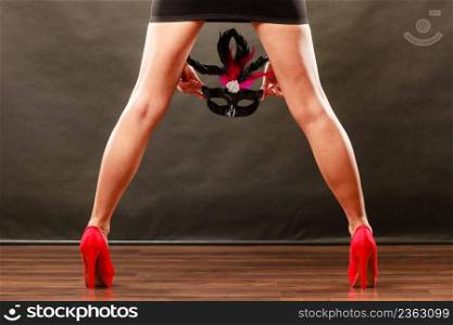 Holidays, people and celebration concept. Woman legs in red high heels and carnival venetian mask on dark.