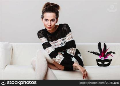Holidays, people and celebration concept. Woman with carnival venetian mask sitting on couch at home
