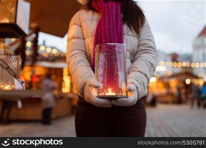 holidays, people and decoration concept - close up of woman with burning candle in lantern at christmas market. woman with candle in lantern at christmas market