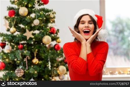 holidays, people and emotions concept - happy smiling young woman in santa helper hat over christmas tree on background. happy young woman in santa hat on christmas