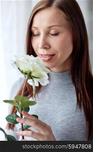 holidays, people and flowers concept - happy young woman smelling big white rose at home