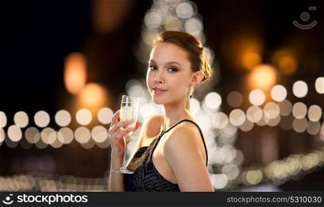 holidays, people and luxury concept - beautiful young asian smiling woman drinking non alcoholic champagne at party over christmas tree lights background. young asian woman drinking champagne at christmas
