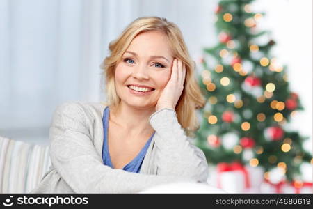 holidays, people, cosiness and leisure concept - happy middle aged woman at home over christmas tree background