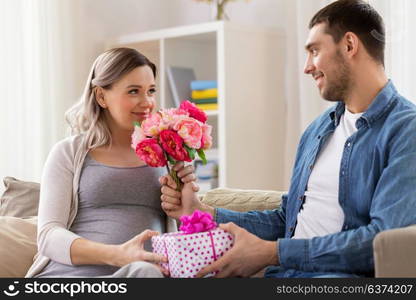 holidays, pregnancy and greetings concept - happy man giving flowers to pregnant woman at home. man giving flowers to pregnant woman at home