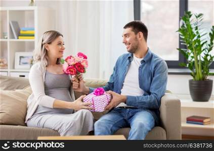 holidays, pregnancy and greetings concept - happy man giving flowers to pregnant woman at home. man giving flowers to pregnant woman at home