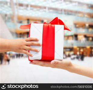 holidays, present, christmas, childhood and happiness concept - close up of child and mother hands with gift box over shopping center background