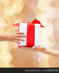 holidays, present, christmas, childhood and happiness concept - close up of child and mother hands with gift box over beige lights background