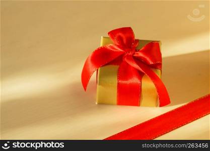 Holidays, present concept. Small golden box with gift tied decorative bow and red ribbon