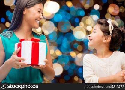 holidays, presents and people concept - happy mother and child girl with gift box over lights background. happy mother and daughter girl with gift box