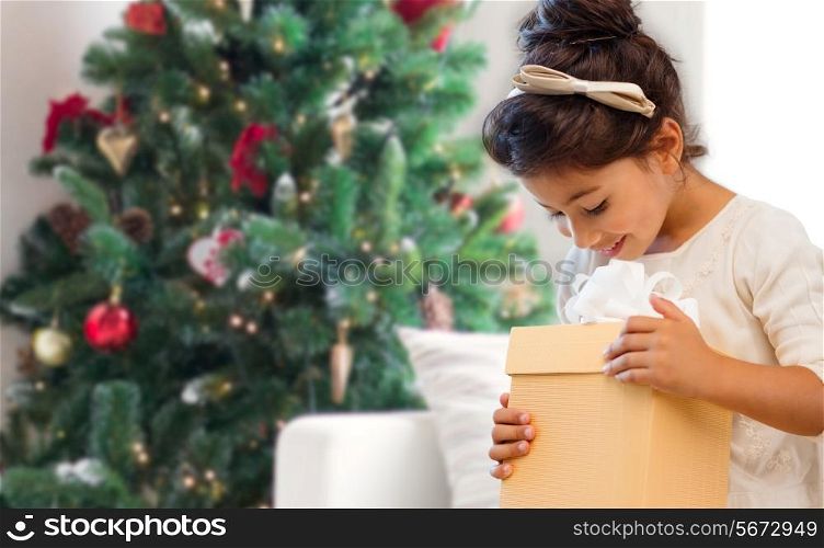 holidays, presents, childhood and people concept - smiling little girl with gift box over living room and christmas thee background