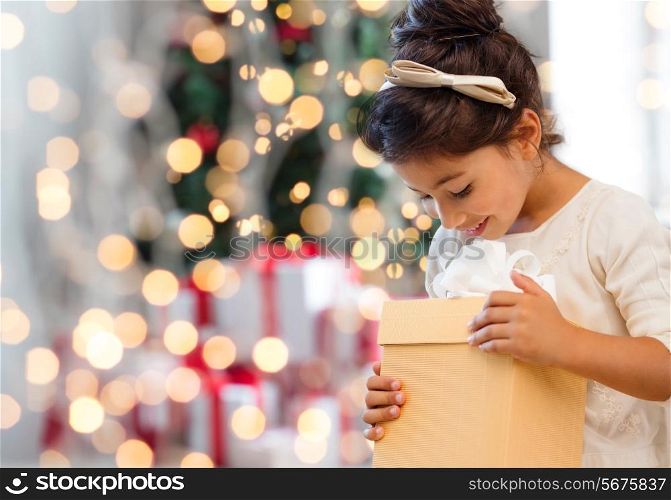 holidays, presents, childhood and people concept - smiling little girl with gift box over living room and christmas thee background