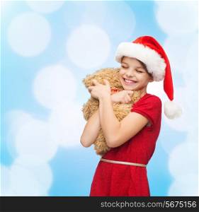 holidays, presents, christmas, childhood and people concept - smiling girl in santa helper hat with teddy bear over blue lights background