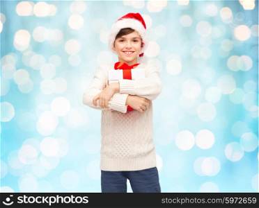 holidays, presents, christmas, childhood and people concept - smiling happy boy in santa hat with gift box over blue holidays lights background