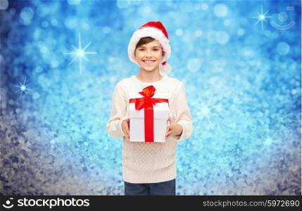 holidays, presents, christmas, childhood and people concept - smiling happy boy in santa hat with gift box over blue holidays lights background